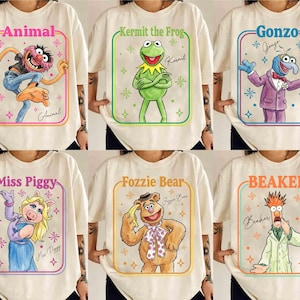 Może przedstawiać: Sześć kremowych koszulek z postaciami z Muppetów: Animal, Kermit Żaba, Gonzo, Miss Piggy, Fozzie Bear i Beaker. Każda koszulka przedstawia ilustrację postaci w kolorowej ramce, z imieniem postaci u góry i podpisem na dole.