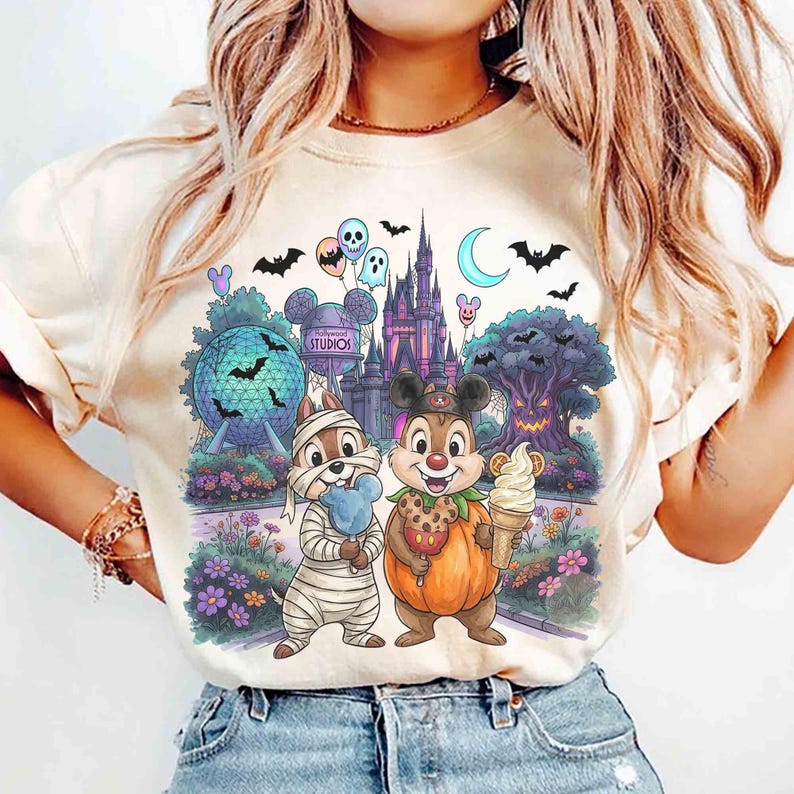 May include: A cream-colored t-shirt featuring a graphic print of two chipmunks in Halloween costumes. One is wrapped like a mummy holding a blue treat, and the other wears a pumpkin outfit holding an ice cream cone, set against a theme park backdrop.