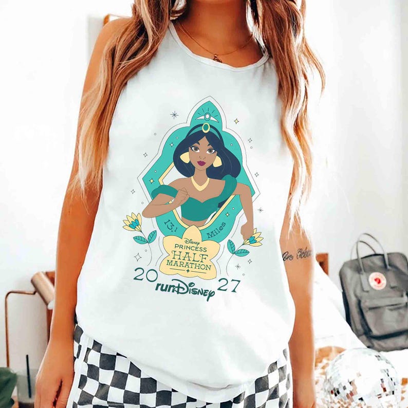 K&ouml;nnte beinhalten: Wei&szlig;es Tanktop mit einer Grafik von Prinzessin Jasmin aus Disneys Aladdin, in T&uuml;rkis und Gold. Das Design enth&auml;lt den Text "Disney Princess Half Marathon" und "13.1 Miles" mit dem Jahr "2027".