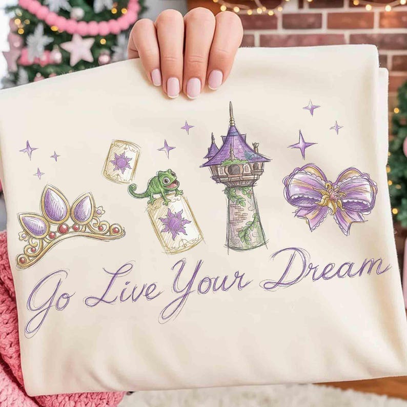 Może przedstawiać: Kremowa tkanina z fioletowymi ilustracjami tiary, wieży i kokardy. Zielony kameleon siedzi na butelce. Tekst "Go Live Your Dream" jest napisany fioletowym skryptem.