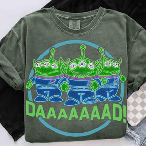 May include: Green crew neck sweatshirt featuring a graphic of three green aliens with blue and purple accents, inside a blue circle. The word "DAAAAAAD!" is printed in green below the aliens. The sweatshirt has a vintage, washed look.