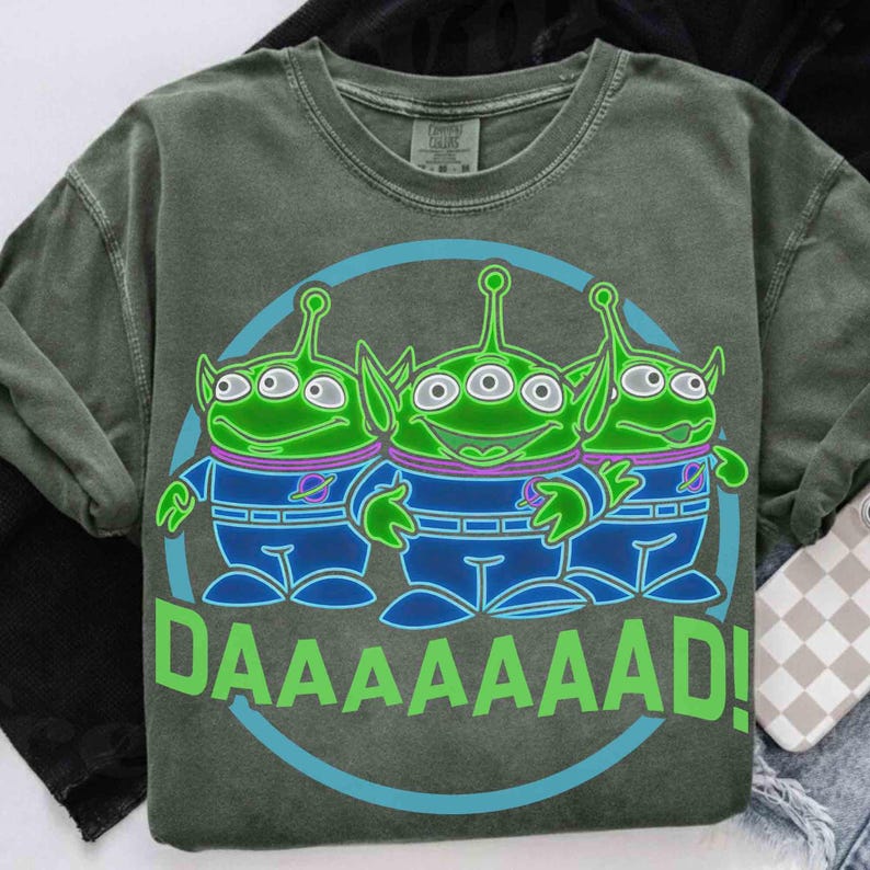 May include: Green crew neck sweatshirt featuring a graphic of three green aliens with blue and purple accents, inside a blue circle. The word "DAAAAAAD!" is printed in green below the aliens. The sweatshirt has a vintage, washed look.