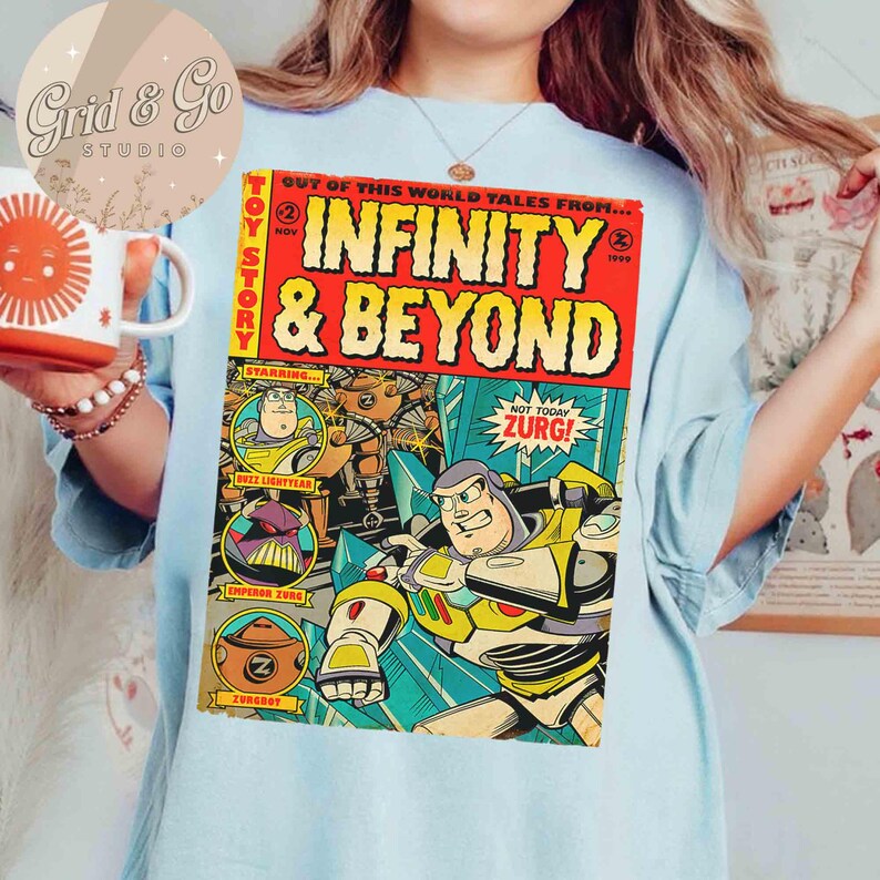 May include: Light blue t-shirt featuring a comic book-style graphic from Toy Story. The graphic reads "INFINITY & BEYOND" with Buzz Lightyear and Zurg. The shirt also has the text "NOT TODAY ZURG!" and "BUZZ LIGHTYEAR".