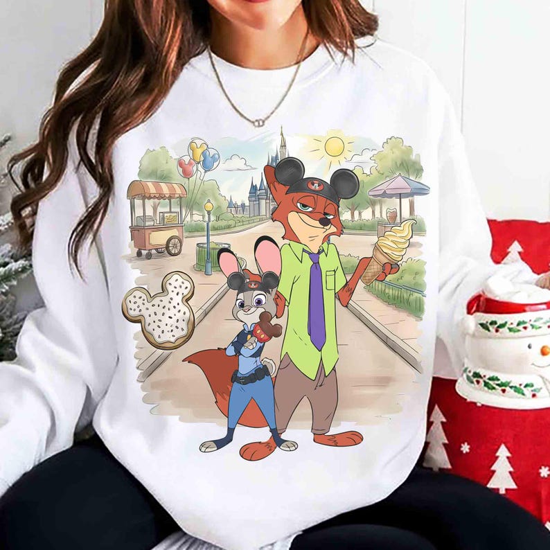 May include: White sweatshirt featuring a cartoon illustration of Nick Wilde and Judy Hopps from Zootopia. The characters are depicted in a park setting with a castle, ice cream, and a Mickey Mouse-shaped donut. The sweatshirt has a crew neck.