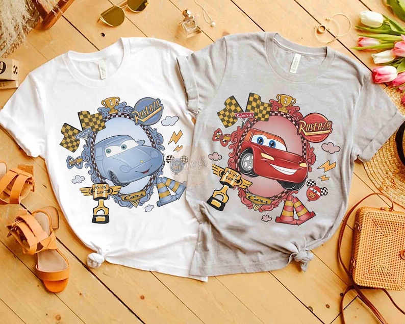 Puede incluir: Dos camisetas con gr&aacute;ficos de coches. Una es blanca con un dise&ntilde;o de coche azul, la otra es gris con un dise&ntilde;o de coche rojo. Cada camiseta presenta un coche de dibujos animados en un marco decorativo.