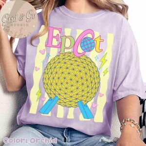Pu&ograve; includere: T-shirt color orchidea con grafica della sfera Epcot e la scritta "Epcot" in rosa, verde e blu. Il design include fulmini e cuori gialli. La maglietta ha una vestibilit&agrave; morbida.