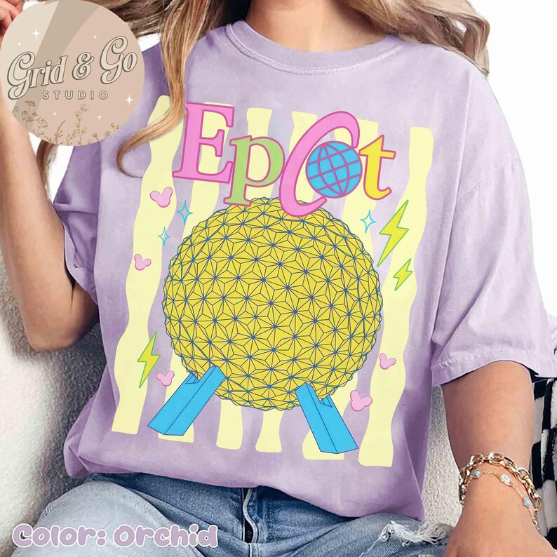 Pu&ograve; includere: T-shirt color orchidea con grafica della sfera Epcot e la scritta "Epcot" in rosa, verde e blu. Il design include fulmini e cuori gialli. La maglietta ha una vestibilit&agrave; morbida.