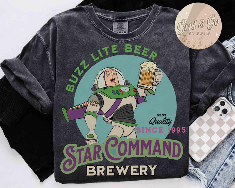 以下が含まれることがあります： バズ・ライトイヤーの漫画がビールジョッキを持っているダークグレーのTシャツ。「Buzz Lite Beer」と「Star Command Brewery」の文字と「Best Quality Since 1995」の文字が入っています。
