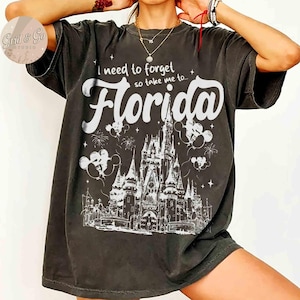 Puede incluir: Camiseta gris oscuro con el texto blanco "I need to forget so take me to... Florida". El dise&ntilde;o incluye una ilustraci&oacute;n detallada de un castillo, fuegos artificiales y siluetas de Mickey Mouse.