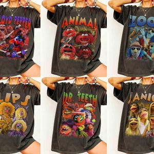 May include: Six dark gray t-shirts featuring Muppets band members. Each shirt displays a different band member's name: Floyd Pepper, Animal, Zoot, Lips, Dr. Teeth, and Janice. The shirts have colorful graphics of the Muppets.