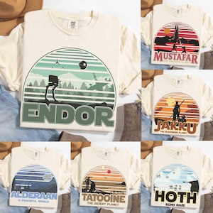 May include: Cream-colored t-shirts with various Star Wars-themed graphics. Designs include landscapes with text like "Endor," "Mustafar," "Jakku," "Alderaan," "Tatooine," and "Hoth." Each graphic features a circular or semi-circular design with a retro aesthetic.