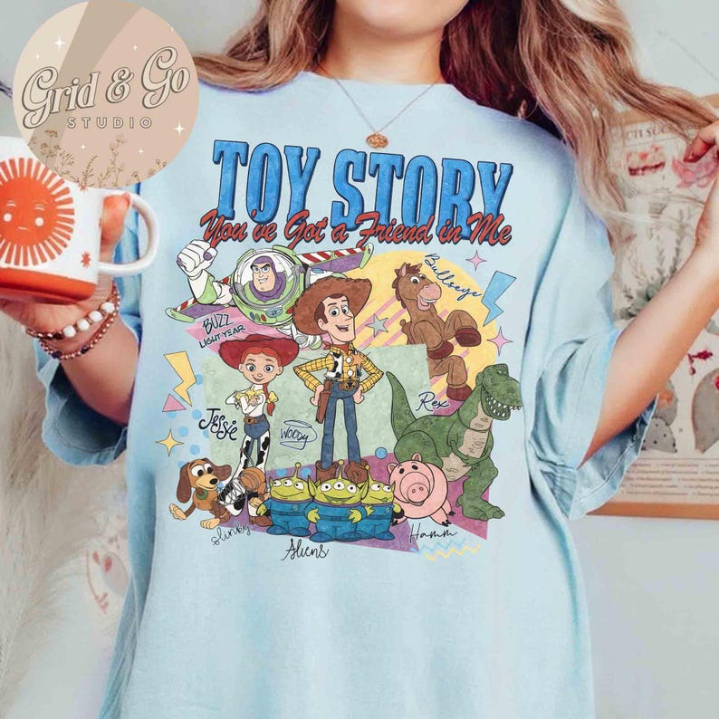 May include: Light blue t-shirt featuring the text "TOY STORY" and "You've Got a Friend in Me". The shirt has a graphic of characters including Buzz Lightyear, Woody, Jessie, Rex, and the Aliens. The shirt is a comfortable, casual wear.