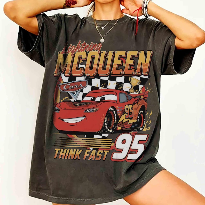 Pu&ograve; includere: T-shirt grigio scuro con Lightning McQueen del film Cars. Il design include il numero 95, le parole "Lightning McQueen" e "Think Fast" e un'auto dei cartoni animati rossa. La grafica &egrave; in rosso, giallo e bianco.