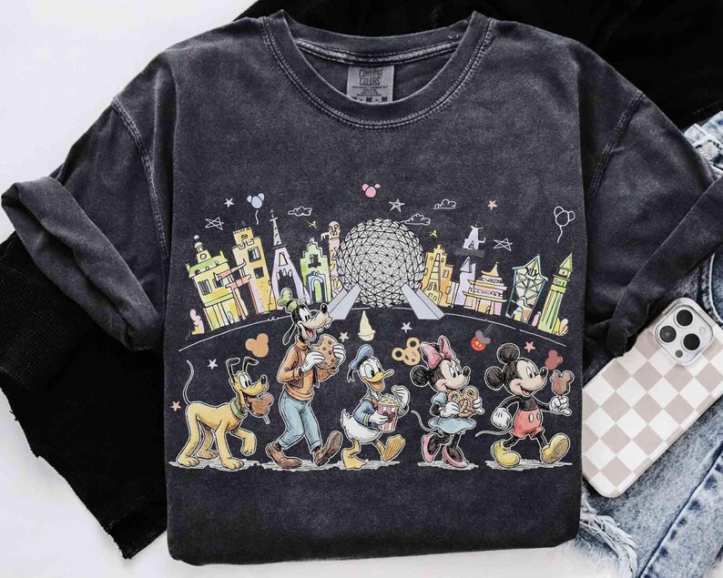 May include: Dark gray t-shirt featuring a colorful graphic of Disney characters, including Mickey Mouse, Minnie Mouse, Goofy, Donald Duck, and Pluto, walking in front of iconic landmarks. The shirt has a vintage, washed look.
