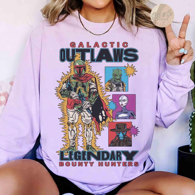 May include: A lilac long-sleeved top with a graphic of a bounty hunter and the text "GALACTIC OUTLAWS LEGENDARY BOUNTY HUNTERS". The graphic includes images of other characters in boxes.