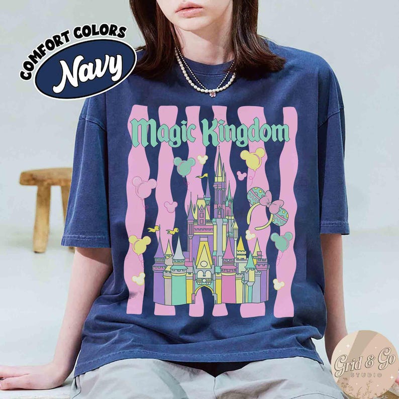 Pu&ograve; includere: T-shirt blu navy con una grafica colorata di un castello, palloncini e la scritta "Magic Kingdom". La maglietta presenta anche la scritta "Comfort Colors Navy" in un design circolare. Il disegno &egrave; stampato su una maglietta a maniche corte.
