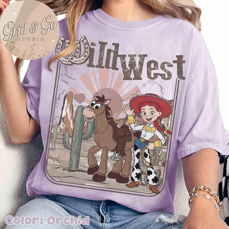 May include: Orchid-coloured t-shirt with a Wild West design. The graphic features a cartoon horse, a cowgirl, cacti, and the text "Wild West." The design is framed by a horseshoe and a heart.