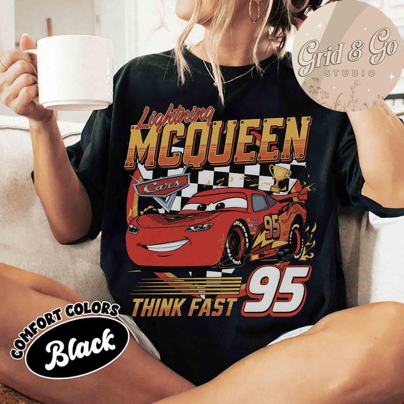Pu&ograve; includere: T-shirt nero con Lightning McQueen del film Cars. Il design include il testo "Lightning McQueen", "Cars", "95" e "Think Fast". La maglietta presenta un'auto Lightning McQueen rossa con uno sfondo a scacchi.