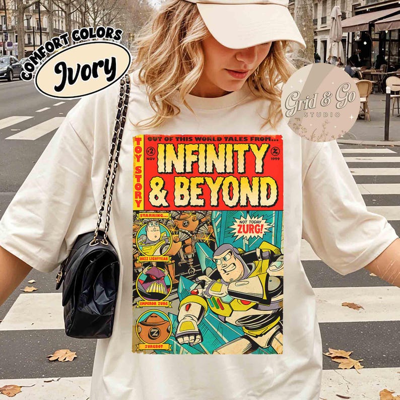 May include: Ivory-colored t-shirt featuring a comic book-style graphic with the text "INFINITY & BEYOND" and characters from Toy Story. The shirt also has the text "COMFORT COLORS" and "Grid & Go STUDIO".