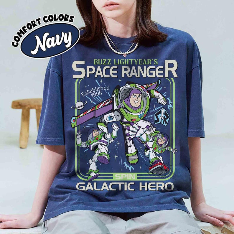 Puede incluir: Camiseta azul marino con un dise&ntilde;o de Buzz Lightyear. El dise&ntilde;o incluye el texto "Buzz Lightyear's Space Ranger" y "Galactic Hero". La camiseta tambi&eacute;n tiene el texto "Comfort Colors" y "Established 1998".