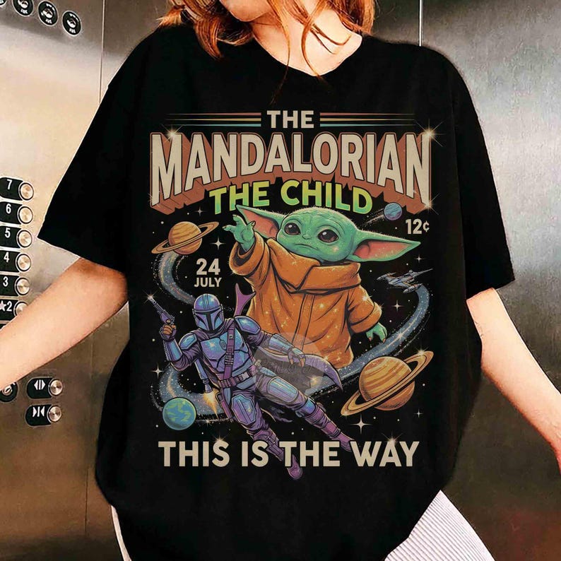 May include: Black t-shirt with a graphic design from The Mandalorian. The design includes the text "THE MANDALORIAN THE CHILD THIS IS THE WAY" with images of the Child, the Mandalorian, and planets.