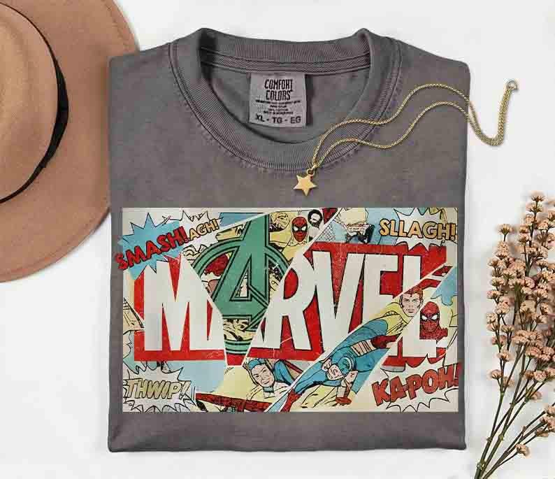 Puede incluir: Camiseta gris con un dise&ntilde;o de c&oacute;mic de Marvel, con el logotipo de Marvel y palabras de c&oacute;mic. Un collar con colgante de estrella dorada descansa sobre la camiseta. Talla XL-TG-EG.