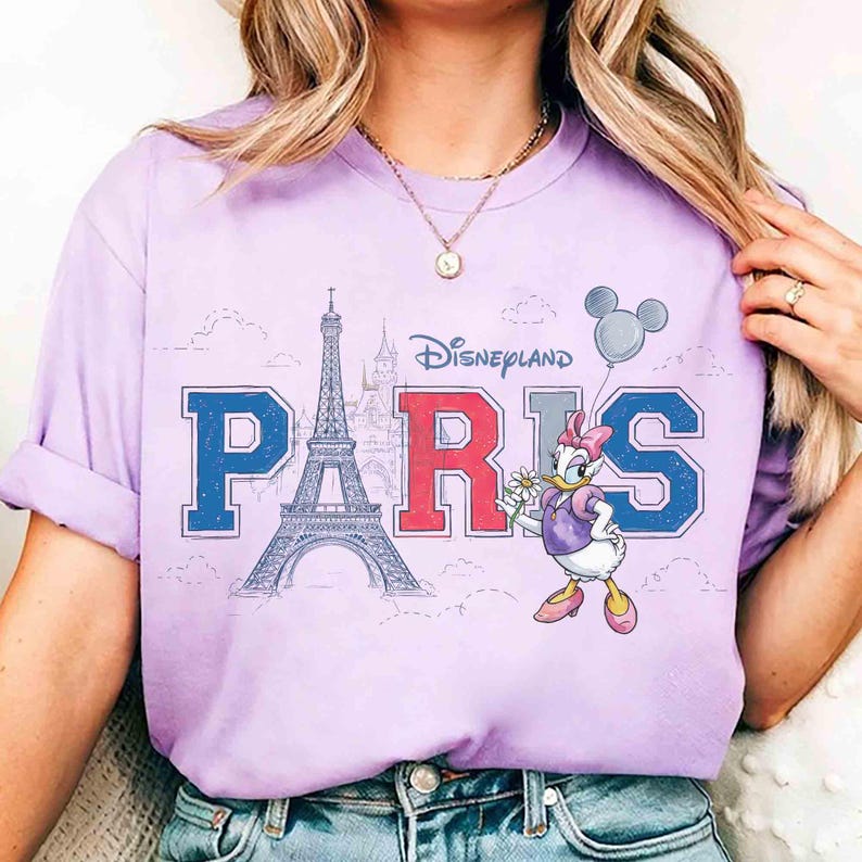 K&ouml;nnte beinhalten: Ein lila T-Shirt mit dem Wort "PARIS" in blauen und roten Blockbuchstaben und der Grafik des Eiffelturms. Das Disneyland-Logo befindet sich &uuml;ber dem Wort. Daisy Duck h&auml;lt eine Blume und einen Mickey Mouse-Ballon.