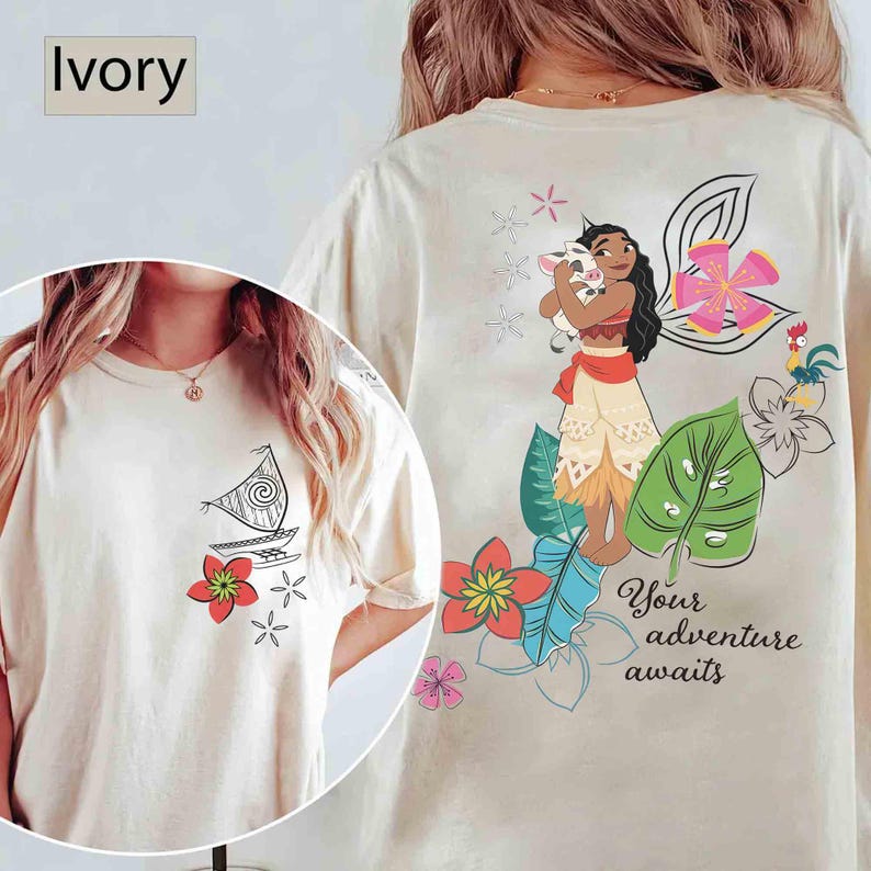 May include: Ivory-colored t-shirt featuring a cartoon illustration of a sailboat and flowers on the front. The back of the shirt displays a character holding a pig, surrounded by flowers and the text "Your adventure awaits."
