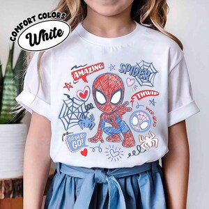 May include: White t-shirt featuring a colorful Spider-Man graphic. The design includes the words "AMAZING" and "SPIDER", along with spider webs, hearts, and the phrases "GO-WEB-GO!" and "WEB-HEAD". The shirt is made of Comfort Colors material.