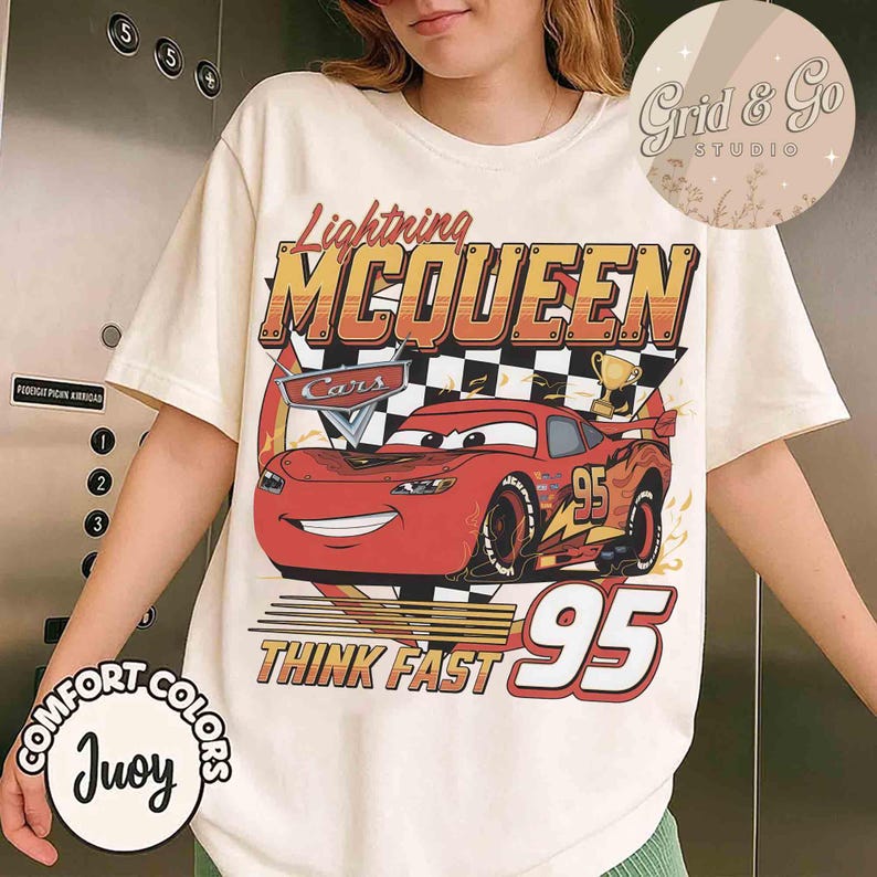 Pu&ograve; includere: T-shirt color crema con grafica di Saetta McQueen del film Cars. Il design include il testo "Lightning McQueen", "Cars", "Think Fast" e il numero "95". La maglietta ha anche il testo "Comfort Colors" e "Juoy".