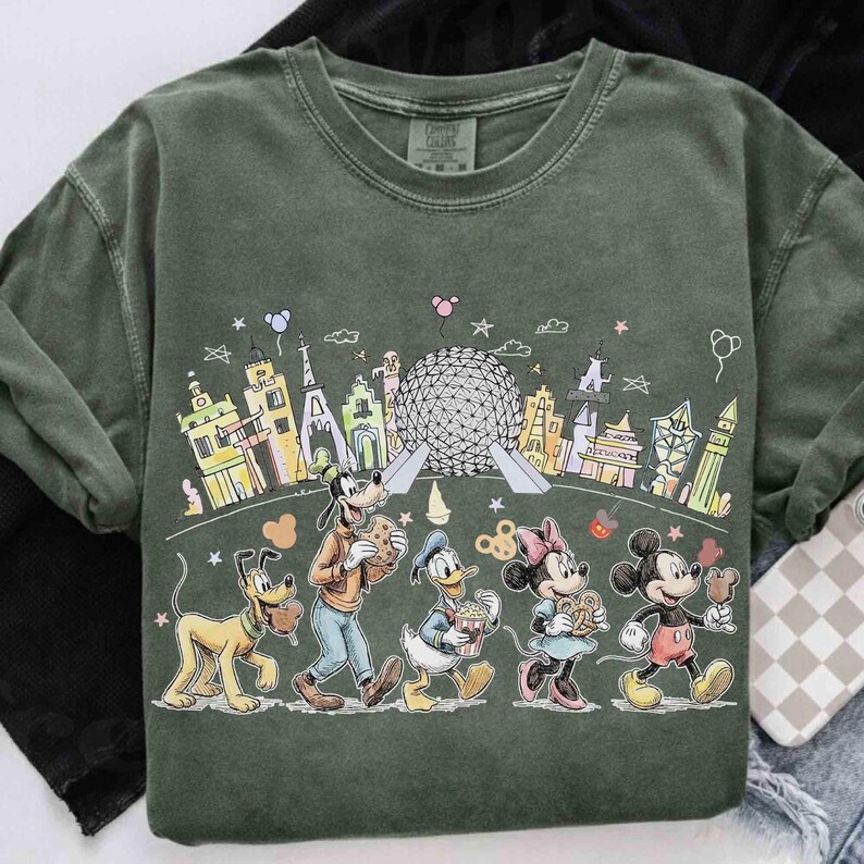 May include: Green crew neck sweatshirt featuring a colorful cartoon illustration of Disney characters walking in front of a cityscape. Pluto, Goofy, Donald Duck, Minnie Mouse, and Mickey Mouse are depicted with snacks.