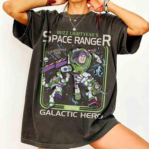Puede incluir: Camiseta gris oscuro con un gr&aacute;fico de Buzz Lightyear's Space Ranger. El dise&ntilde;o incluye a Buzz Lightyear con un traje espacial verde y blanco, con el texto "Established 1998" y "Galactic Hero".