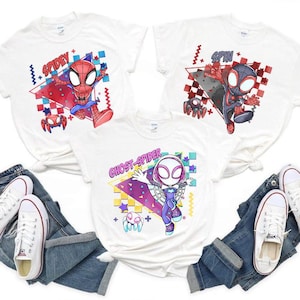 May include: Three white short-sleeved t-shirts featuring cartoon graphics of Spidey, Spin, and Ghost-Spider. Each shirt displays the character name in bold text, accompanied by colourful geometric shapes, checkered patterns, and small spider icons.