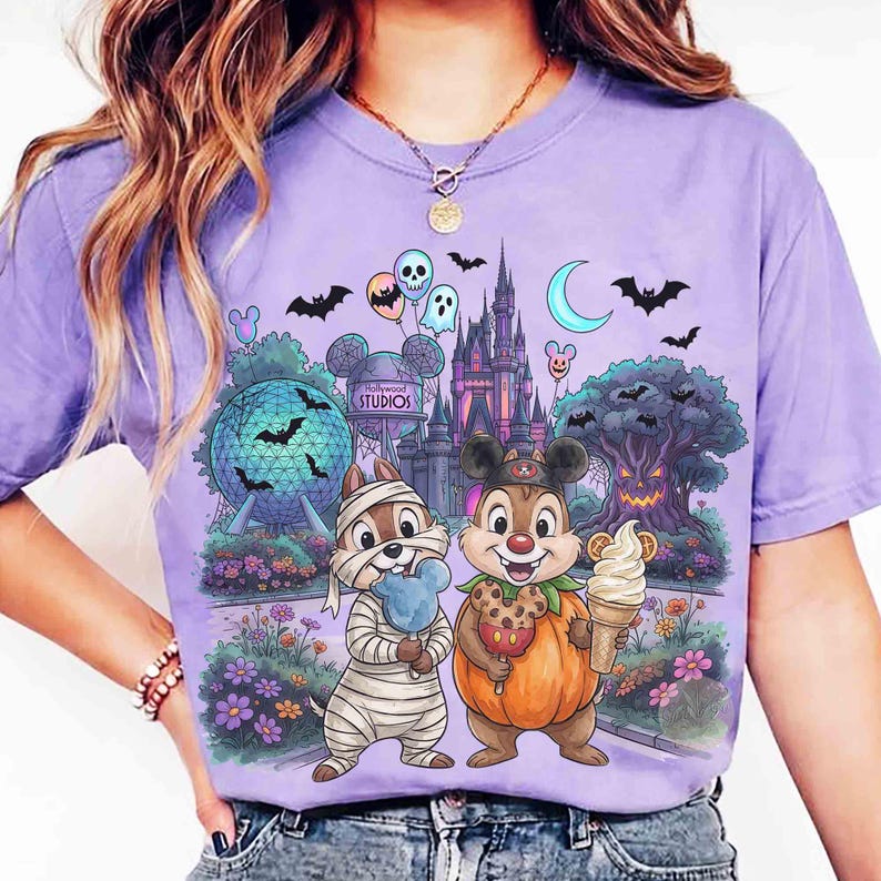 May include: A light purple t-shirt featuring a graphic print of two chipmunks in Halloween costumes, one as a mummy and one as a pumpkin, standing before a theme park castle, a geodesic sphere, and a spooky tree with bats, balloons, and text.