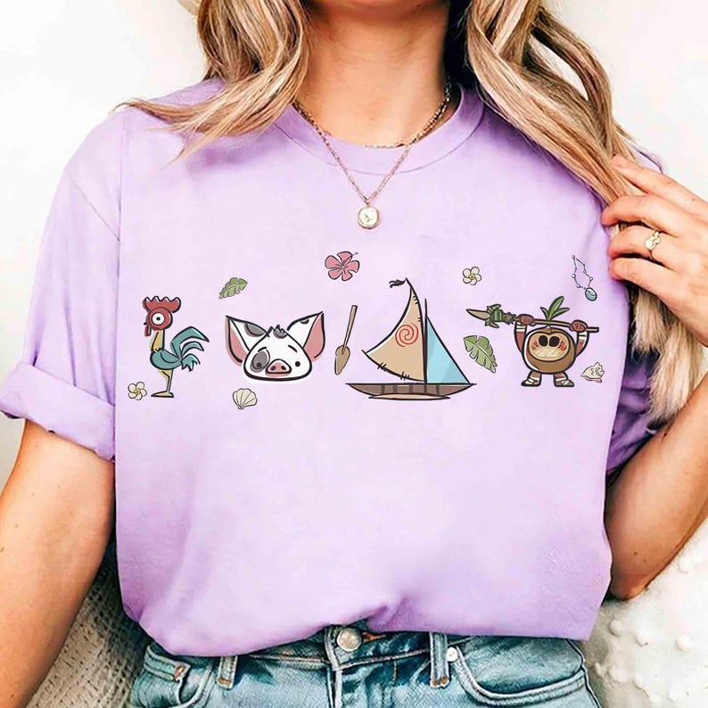 Puede incluir: Una camiseta de manga corta color morado claro con un estampado gr&aacute;fico de un gallo, una cara de cerdo, un remo de madera, un velero con vela en espiral y una peque&ntilde;a criatura de coco con una lanza, decorada con flores y hojas tropicales.