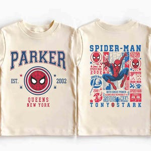 K&ouml;nnte beinhalten: Cremefarbenes T-Shirt mit Spider-Man-Design. Die Vorderseite zeigt "PARKER" in Blau, ein Spider-Man-Emblem und "QUEENS NEW YORK". Die R&uuml;ckseite zeigt Spider-Man in Aktion, mit Text wie "SPIDER-MAN" und "TONY STARK".