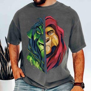 May include: Gray t-shirt featuring a split lion design. One side is green and blue, the other is red and yellow. The graphic is a stylized illustration of a lion's face, with detailed eyes and fur.