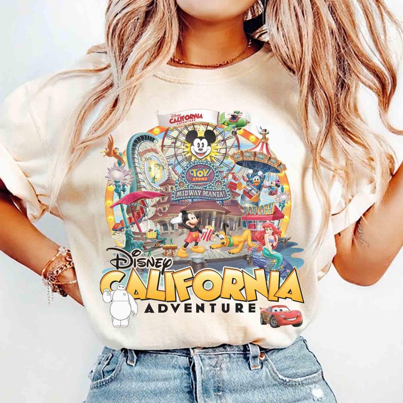 May include: Cream-colored t-shirt featuring a colorful graphic of Disney California Adventure. The design includes Mickey Mouse, a Ferris wheel, and various Disney characters. The words "Disney California Adventure" are prominently displayed.