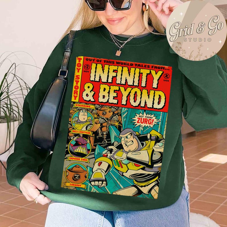 May include: Dark green sweatshirt featuring a comic book-style graphic with the text "INFINITY & BEYOND" and "TOY STORY". The graphic includes Buzz Lightyear and Zurg characters. The sweatshirt has a crew neck and long sleeves.