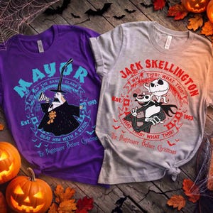 K&ouml;nnte beinhalten: Zwei T-Shirts mit Halloween-Motiven. Eines ist lila mit dem Text "MAYOR" und einer Charakterillustration. Das andere ist grau mit dem Text "JACK SKELLINGTON" und Charakterkunst. K&uuml;rbisse und Bl&auml;tter umgeben die Shirts.