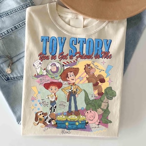 May include: Cream-colored Toy Story graphic t-shirt featuring Buzz Lightyear, Woody, Jessie, Rex, Slinky, Bullseye, Hamm, and the Aliens. The shirt has the text "TOY STORY You've Got a Friend in Me" in blue and red.