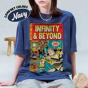 May include: Navy blue t-shirt with a comic book-style graphic featuring Buzz Lightyear and the text "INFINITY & BEYOND." The shirt also has the text "COMFORT COLORS" and "TOY STORY." The graphic is in red, yellow, and blue.