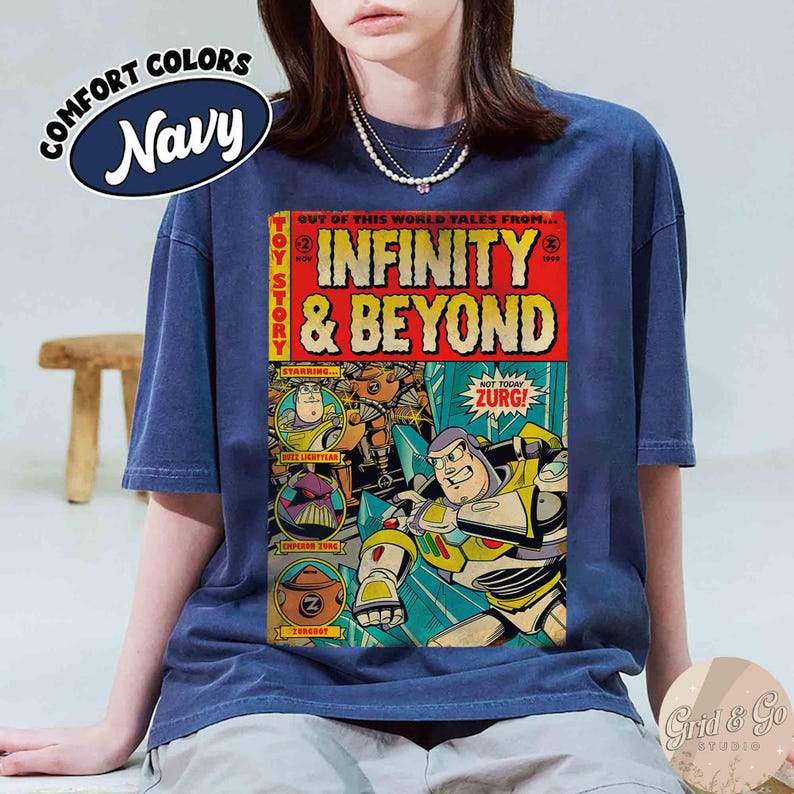 May include: Navy blue t-shirt with a comic book-style graphic featuring Buzz Lightyear and the text "INFINITY & BEYOND." The shirt also has the text "COMFORT COLORS" and "TOY STORY." The graphic is in red, yellow, and blue.