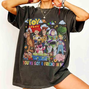 May include: Dark grey t-shirt with a vibrant Toy Story character design, including Woody, Buzz Lightyear, and Jessie. The words "TOY STORY" and "YOU'VE GOT A FRIEND IN ME" are displayed. A casual, fun t-shirt.