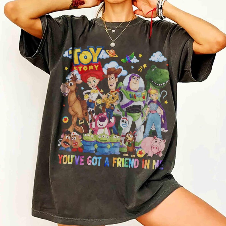 May include: Dark grey t-shirt with a vibrant Toy Story character design, including Woody, Buzz Lightyear, and Jessie. The words "TOY STORY" and "YOU'VE GOT A FRIEND IN ME" are displayed. A casual, fun t-shirt.
