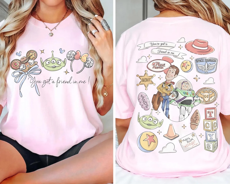 Op de afbeelding: Roze T-shirt met een afbeelding van stripfiguren op de voorkant en de tekst "You got a friend in me!". De achterkant van het shirt heeft meer stripfiguren en tekst.