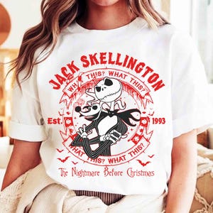 K&ouml;nnte beinhalten: Wei&szlig;es T-Shirt mit roter Grafik von Jack Skellington aus "The Nightmare Before Christmas". Das Design enth&auml;lt den Text "Jack Skellington", "What This?" und "Est. 1993". Das Shirt hat kurze &Auml;rmel.