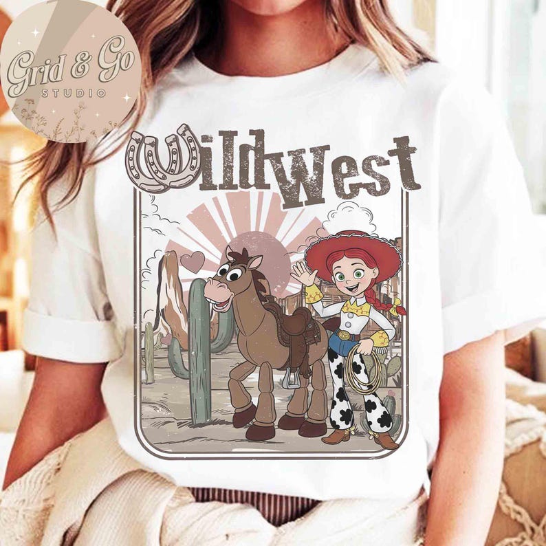 May include: White t-shirt with a Wild West illustration of a cartoon cowgirl, horse, and cactus. The design includes the text "Wild West". The shirt has a crew neck and short sleeves.