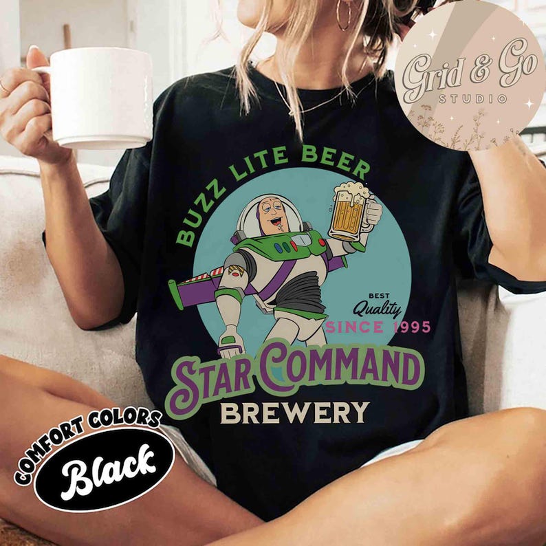 以下が含まれることがあります： 黒いTシャツ。宇宙レンジャーの漫画がビールジョッキを持っています。Tシャツには「BUZZ LITE BEER STAR COMMAND BREWERY」と書かれており、「BEST QUALITY SINCE 1995」と「COMFORT COLORS Black」がプリントされています。