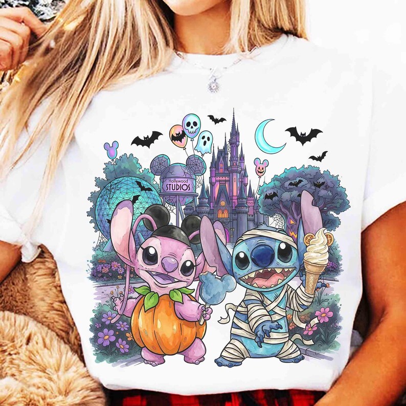 K&ouml;nnte beinhalten: Ein wei&szlig;es T-Shirt mit einem Grafikdruck von zwei blauen und rosafarbenen au&szlig;erirdischen Charakteren in Halloween-Kost&uuml;men. Eine Figur tr&auml;gt ein K&uuml;rbiskost&uuml;m, die andere ist in Bandagen gewickelt. Im Hintergrund sind ein Schloss und Flederm&auml;use zu sehen.